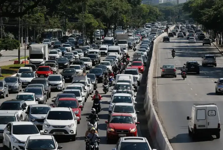 Rodovia com trânsito intenso de carros e motos em um dos sentidos e fluxo livre no sentido oposto.