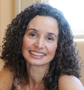 Priscila Prado, autora do livro. Priscila tem pela clara e cabelos médios castanhos cacheados. Sorri.