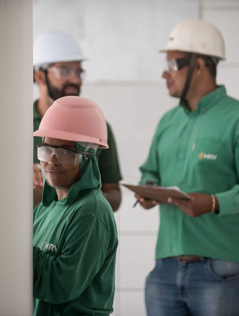 três pessoas em pé com capacete de obra e camisas verdes