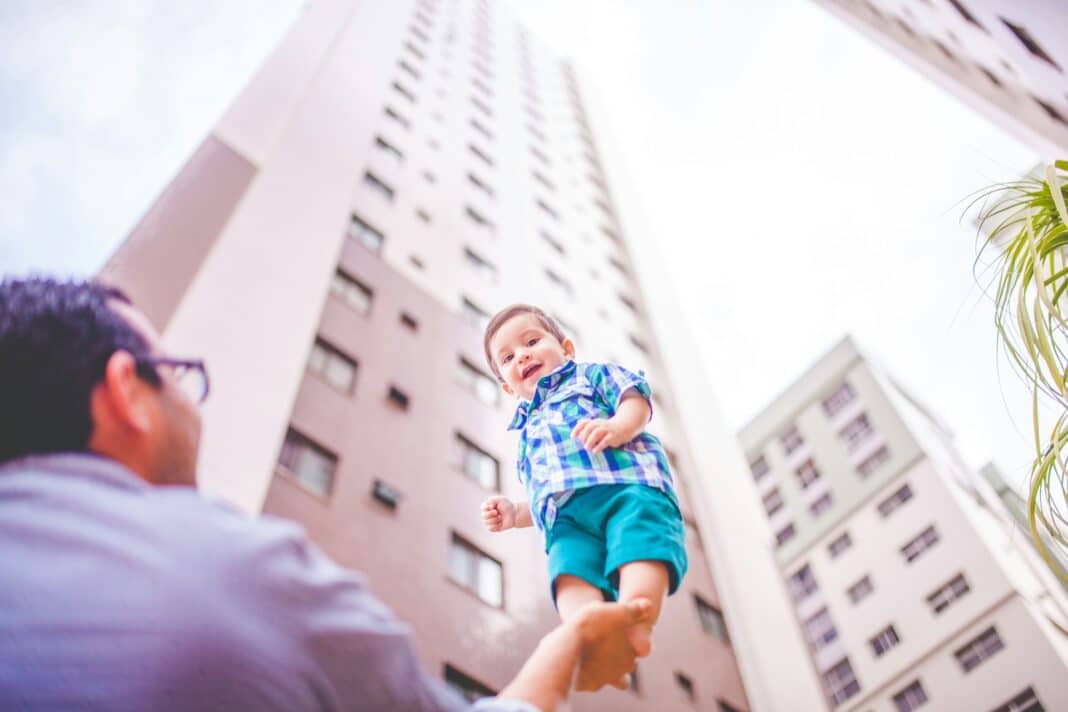 Pai segurando um filho com uma mão ao fundo um prédio