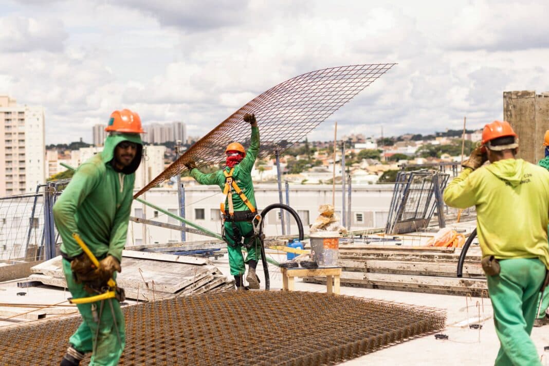 três trabalhadores em um canteiro de obra manipulando arames